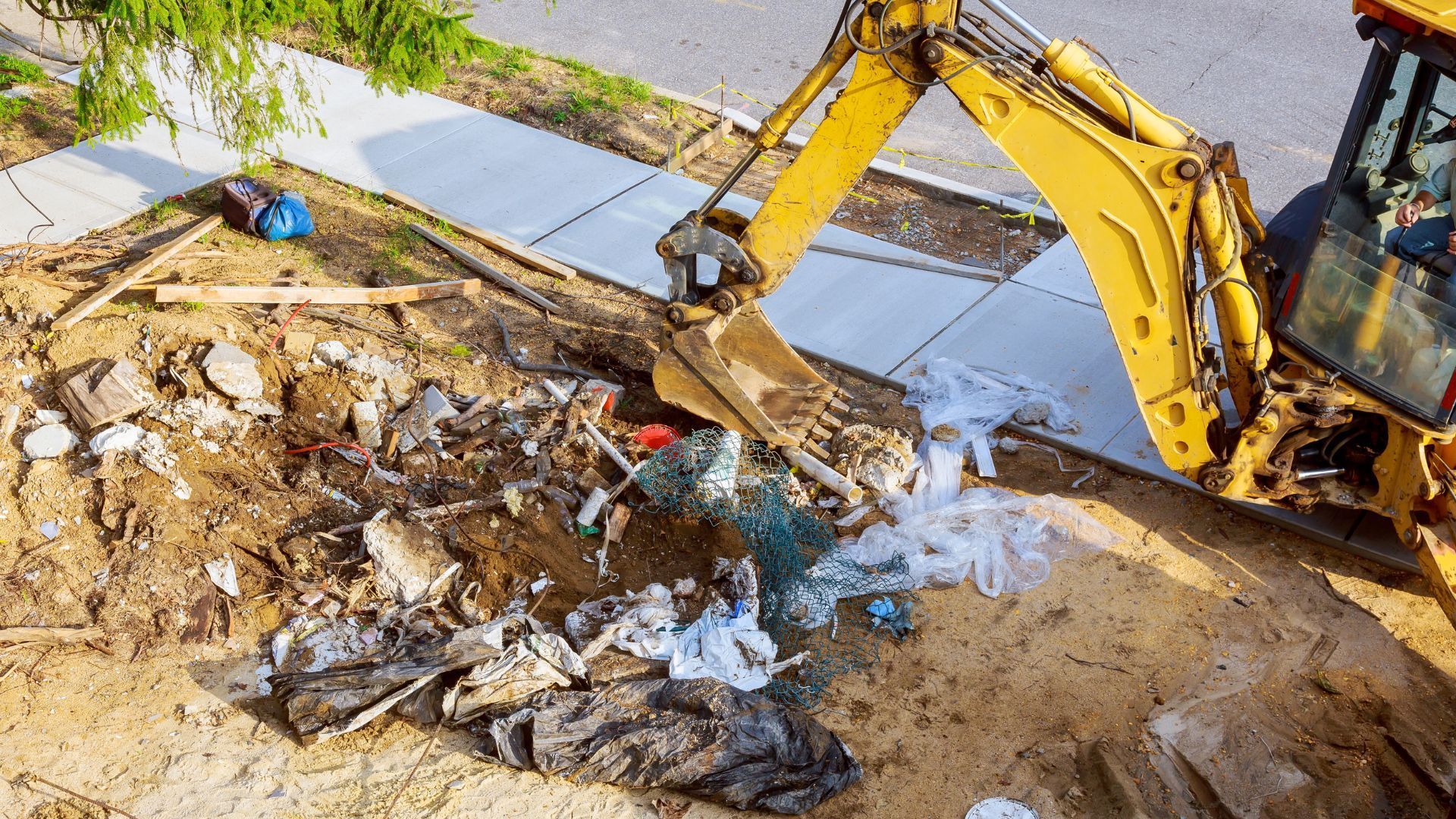Yellow excavator removing debris from a construction site next to a sidewalk.