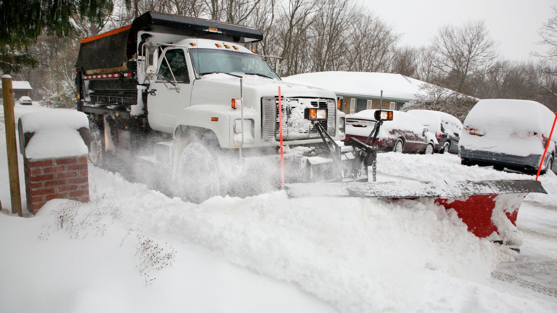 Snowplow clearing snow from a driveway, in front of a house.