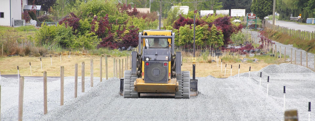 A yellow skid steer tractor on a gravel-covered construction site with wooden stakes.