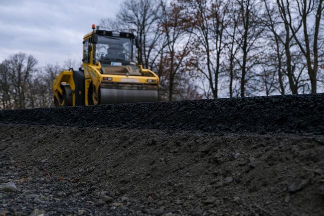 Yellow road roller compacts fresh asphalt on a construction site.