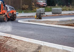Asphalt paving in progress: Roller compacts fresh asphalt. A vibratory plate and pavers are also present.