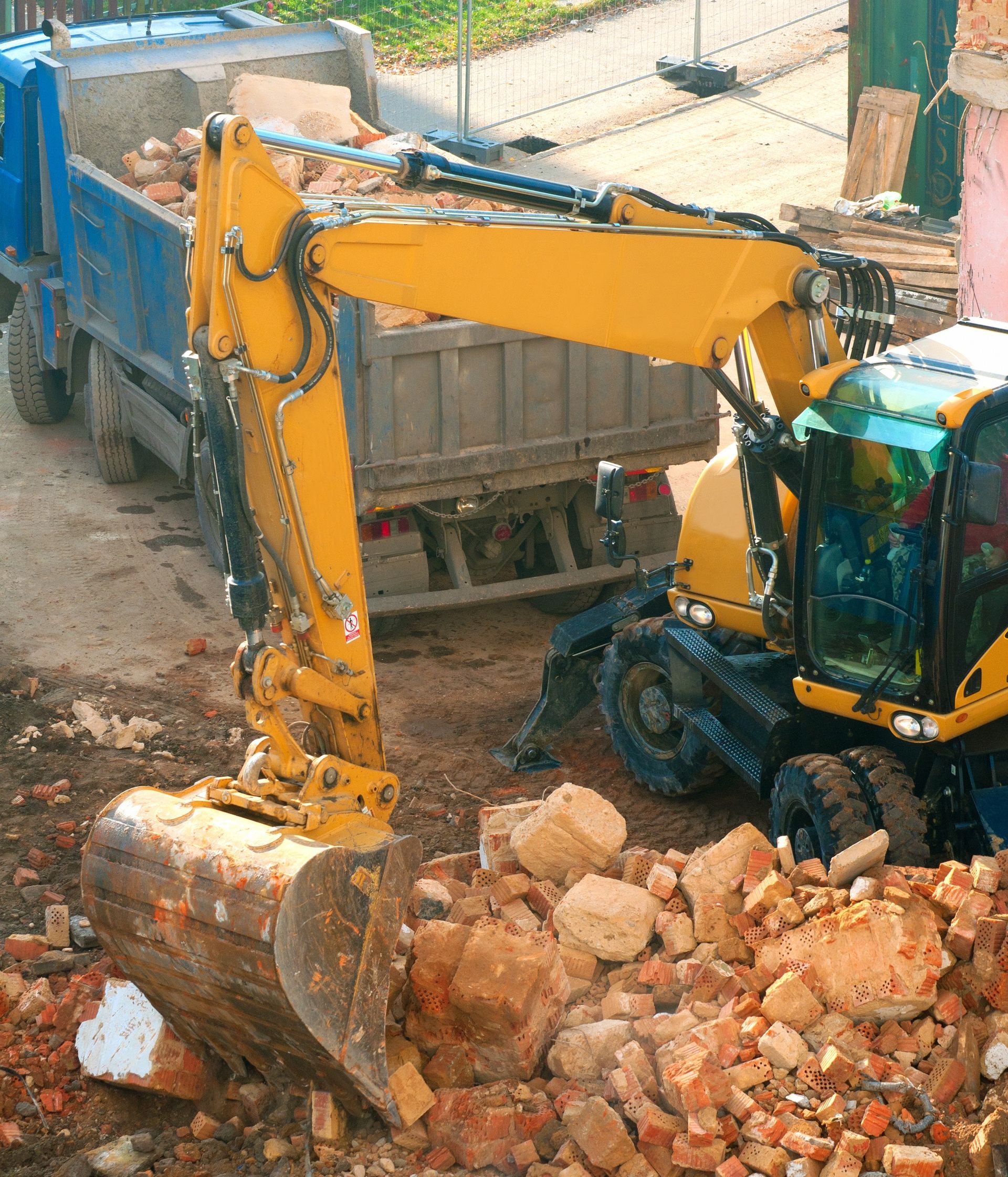 Yellow excavator loading debris into a blue dump truck outdoors.