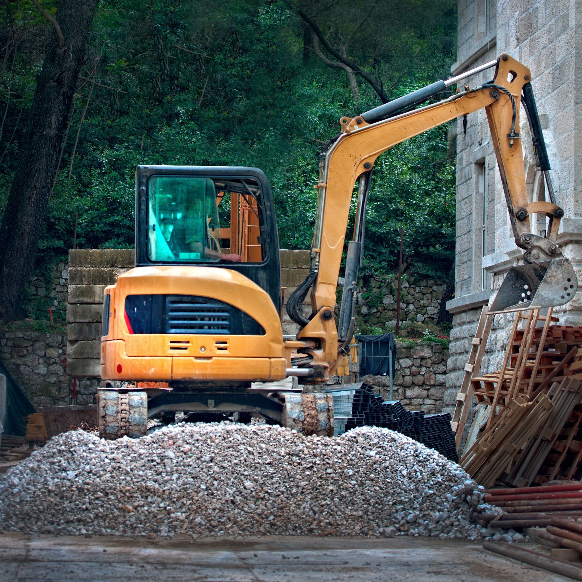 Yellow excavator at a construction site, scooping gravel, near a building.