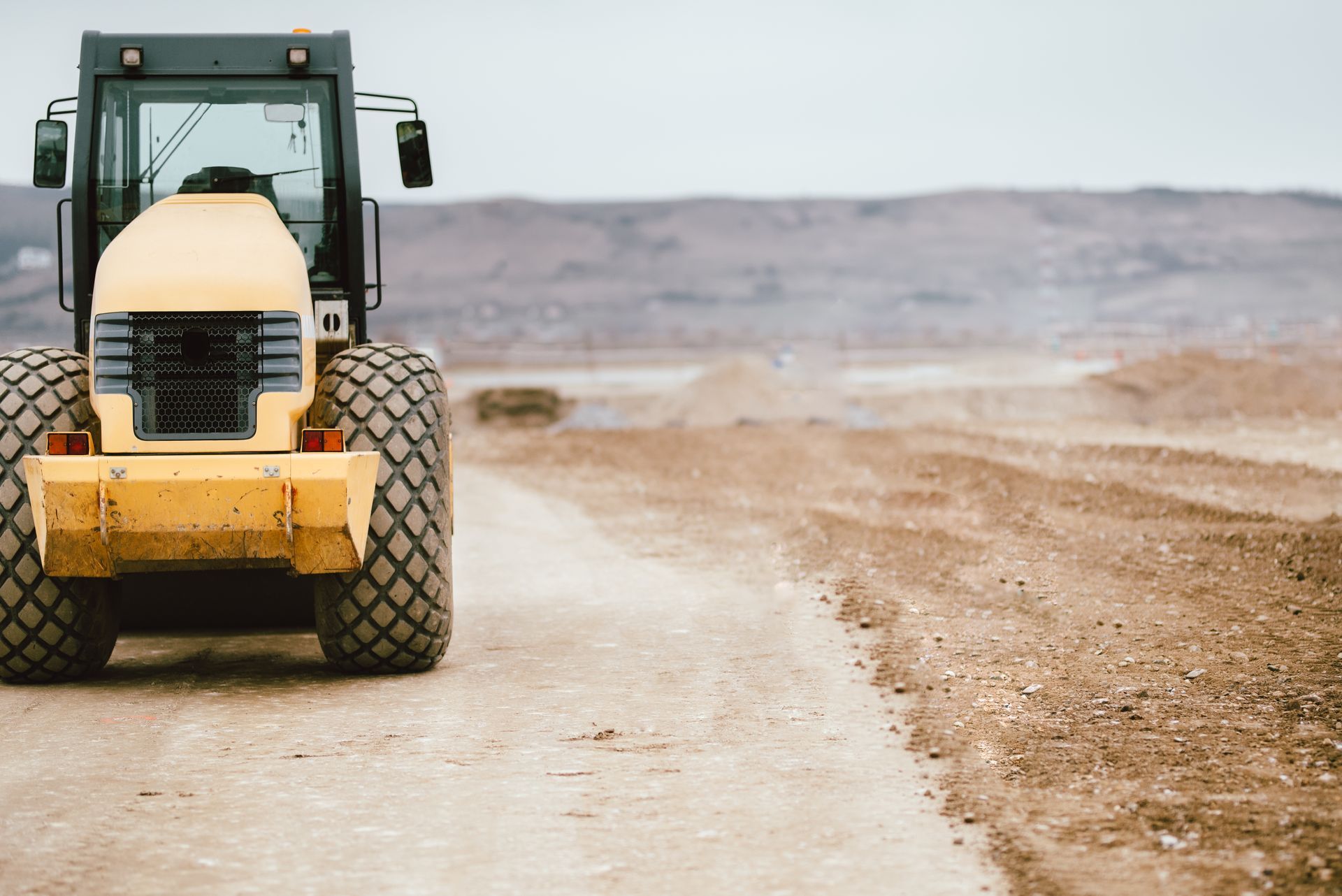 Yellow road roller on a dirt road, flattening the ground at a construction site.