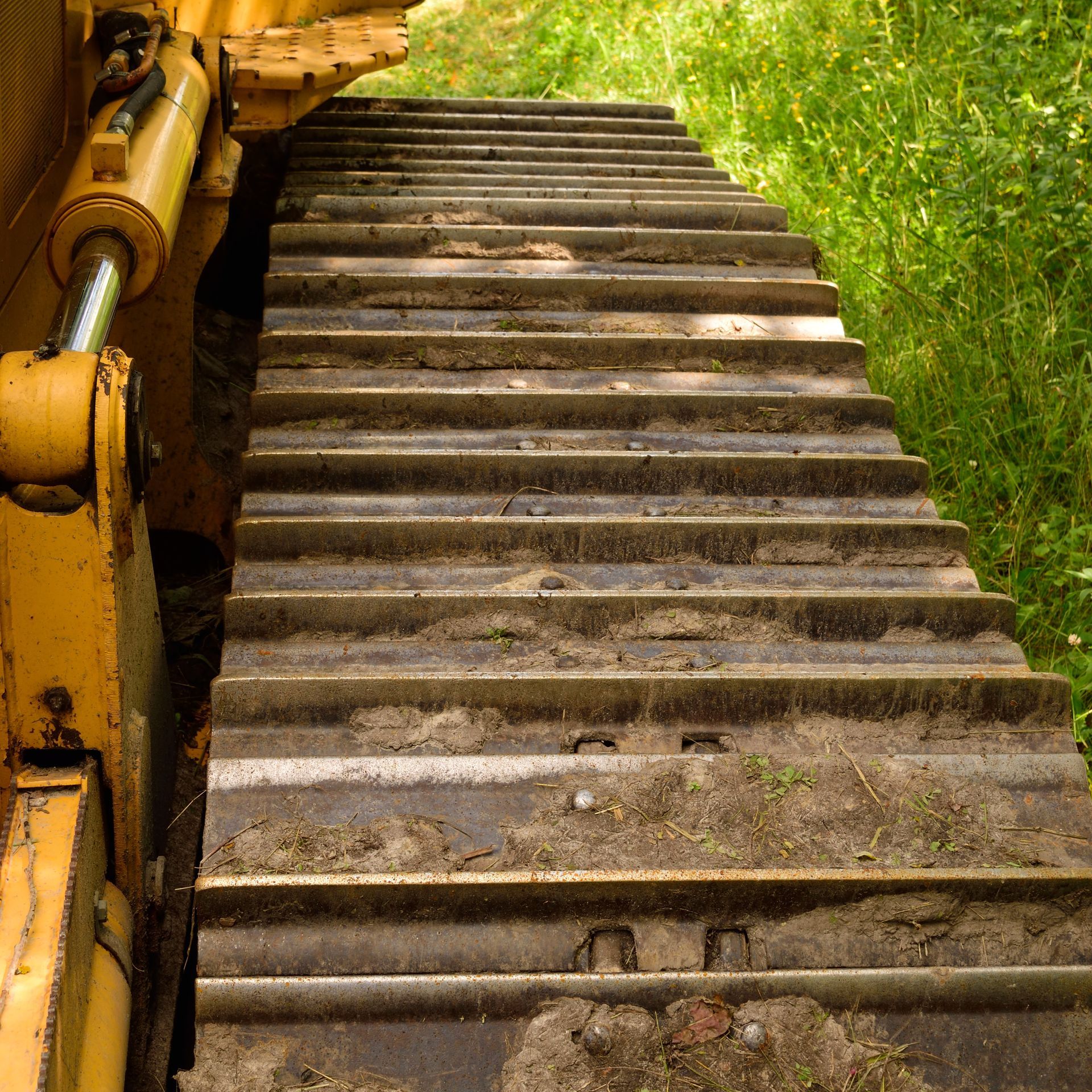 Close-up of a yellow bulldozer track, dirty with earth, next to green grass.