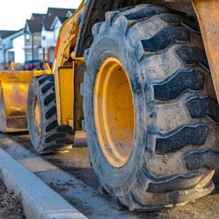 Yellow construction loader parked on a curb; residential homes in the background.