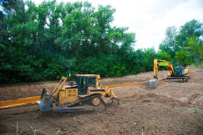 Two yellow construction vehicles grading dirt in a wooded area.