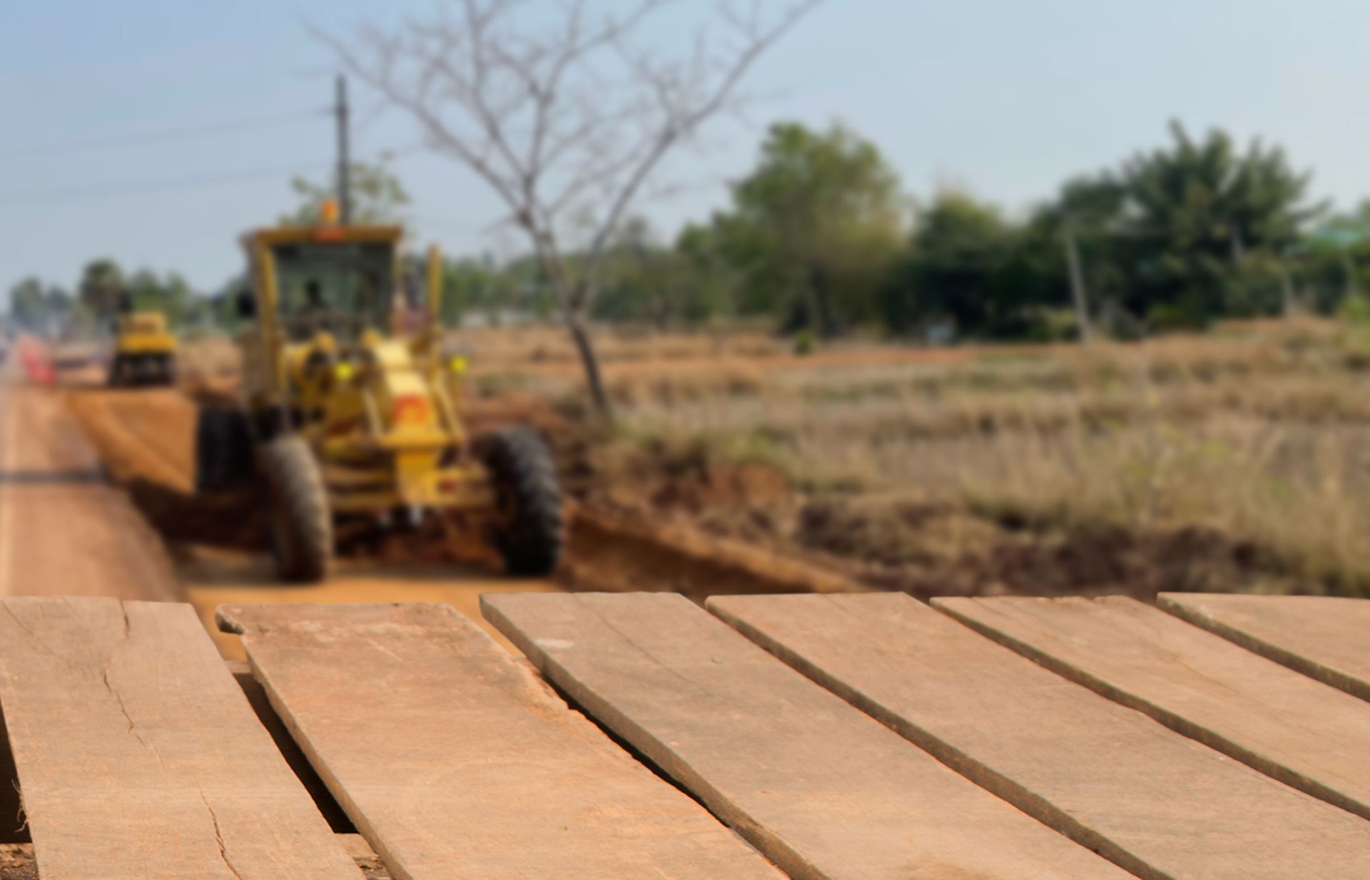 Yellow grader on a dirt road, leveling the ground; construction site, sunny day.