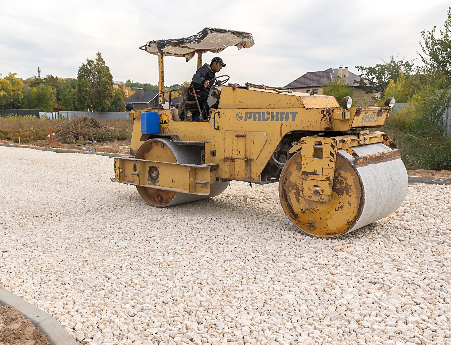 Yellow road roller compacting gravel, with a person driving it.
