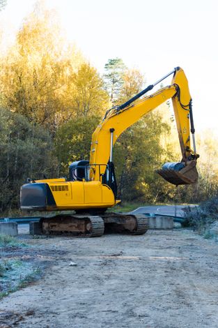 Yellow excavator on gravel in front of trees.