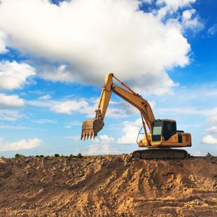 Yellow excavator on a dirt mound under a blue sky with fluffy white clouds.