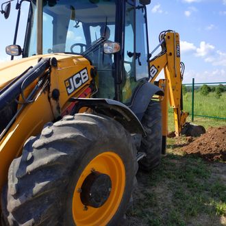 Yellow JCB backhoe digging in a grassy field on a sunny day.