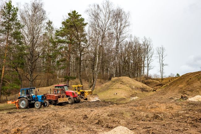 Four tractors on a muddy worksite clearing land in front of a forest.