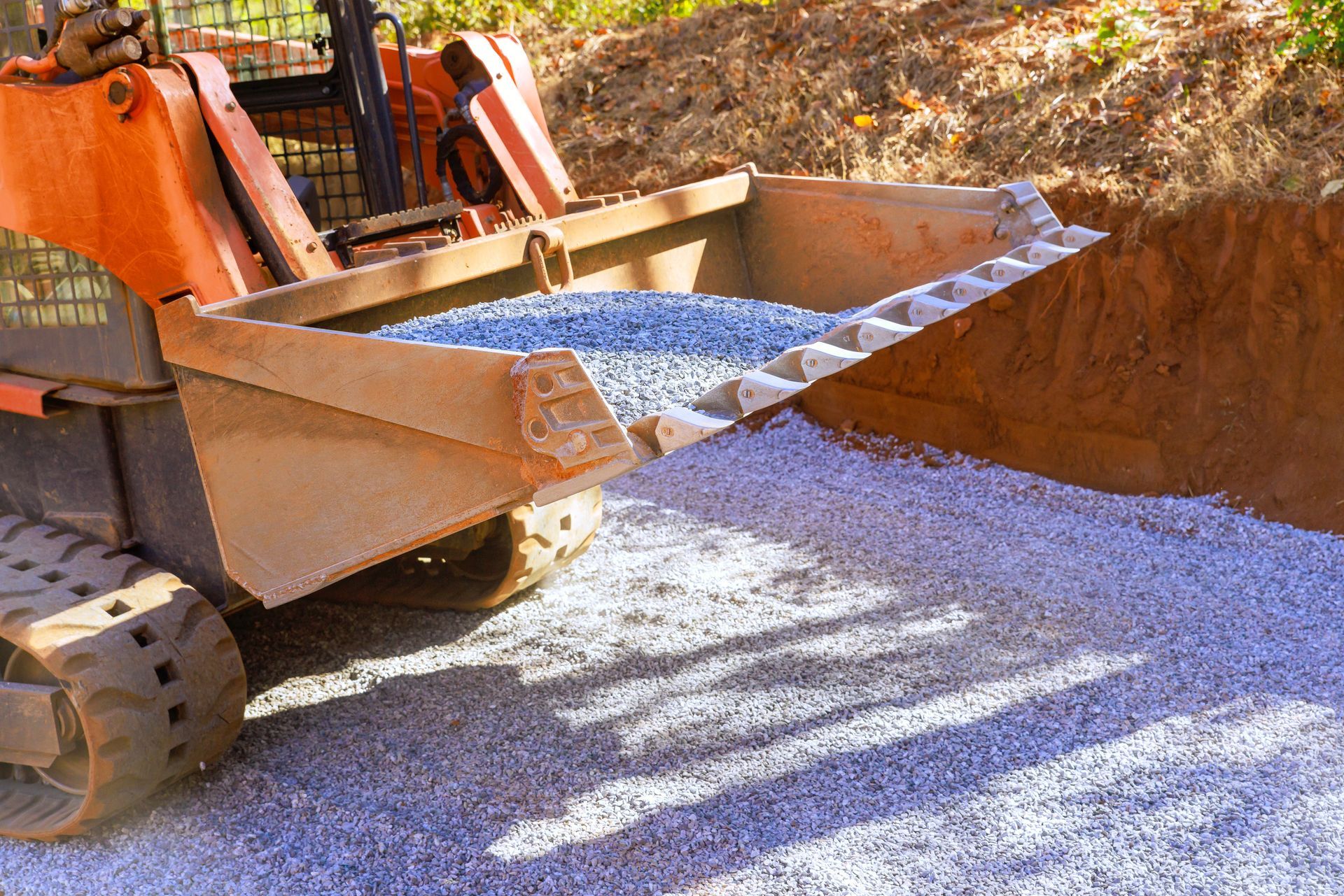 Orange skid steer dumping gravel on a prepared surface at a construction site.