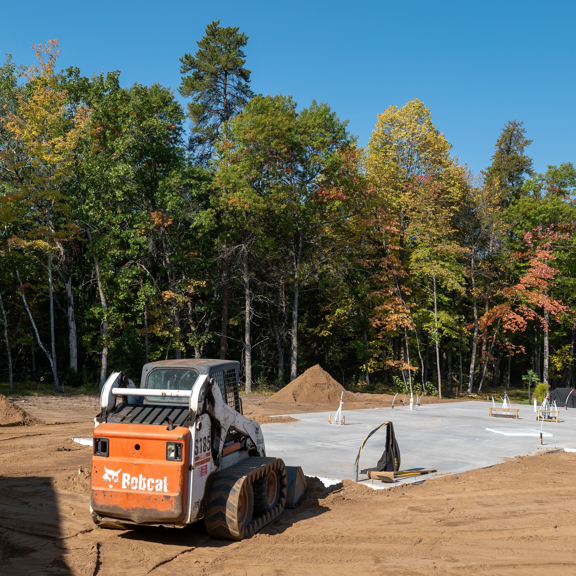 Orange Bobcat on a construction site with trees in the background. Sunny day.