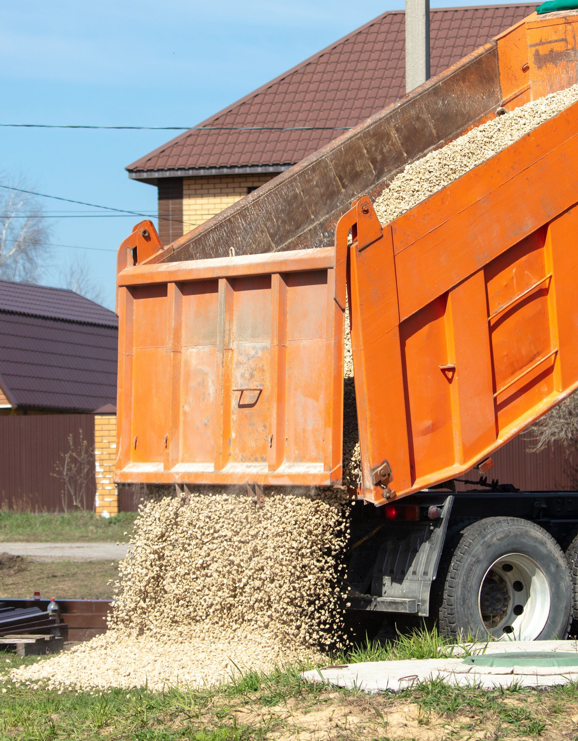 Orange dump truck unloading gravel near a house.