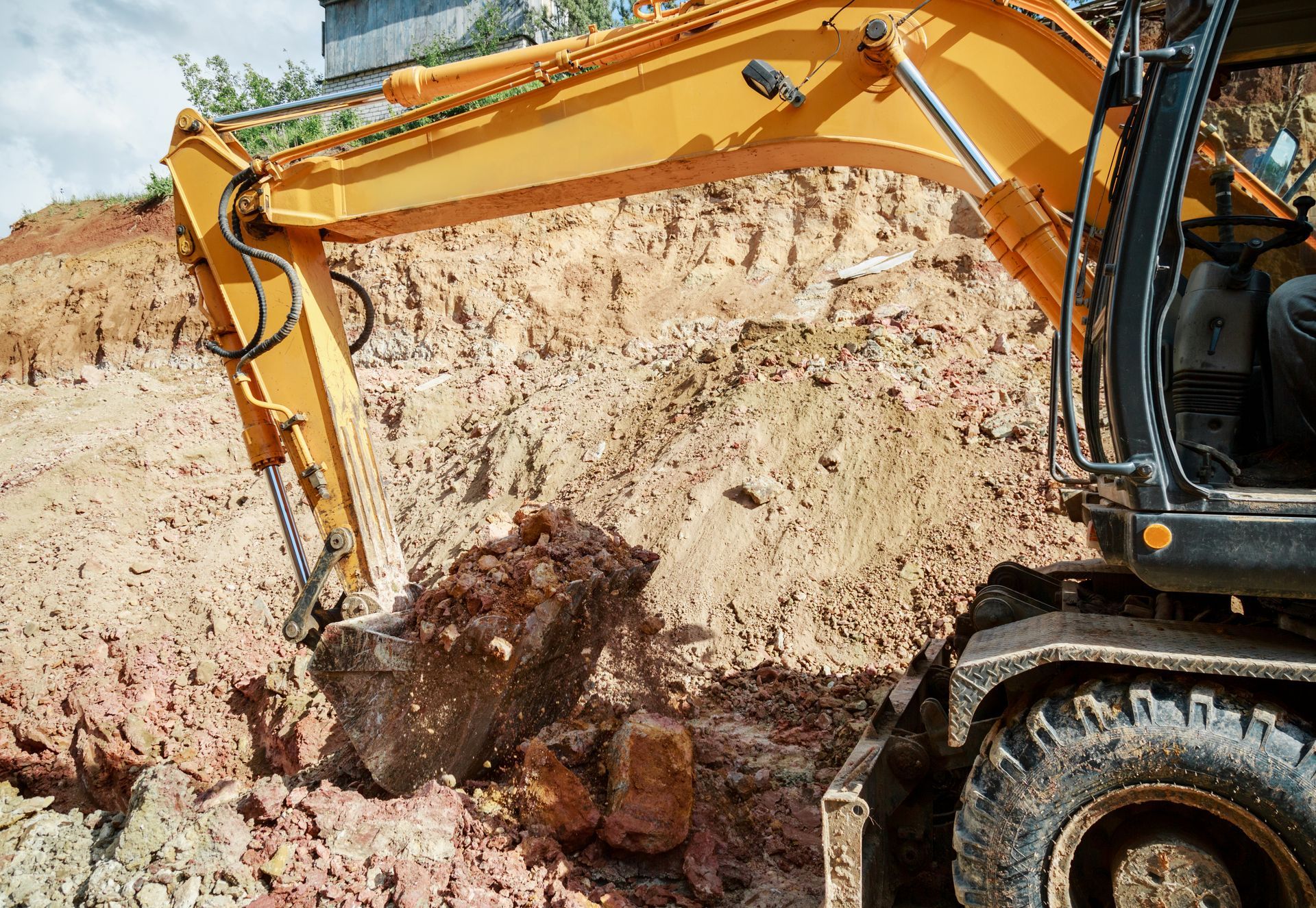 Yellow excavator digging into a dirt wall, scooping up brown soil.