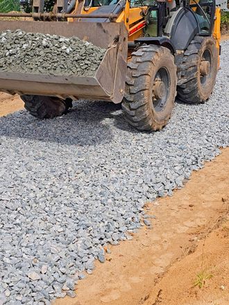 Front-end loader dumping gravel on a roadbed. Construction vehicle on dirt, gray gravel, and brown soil.