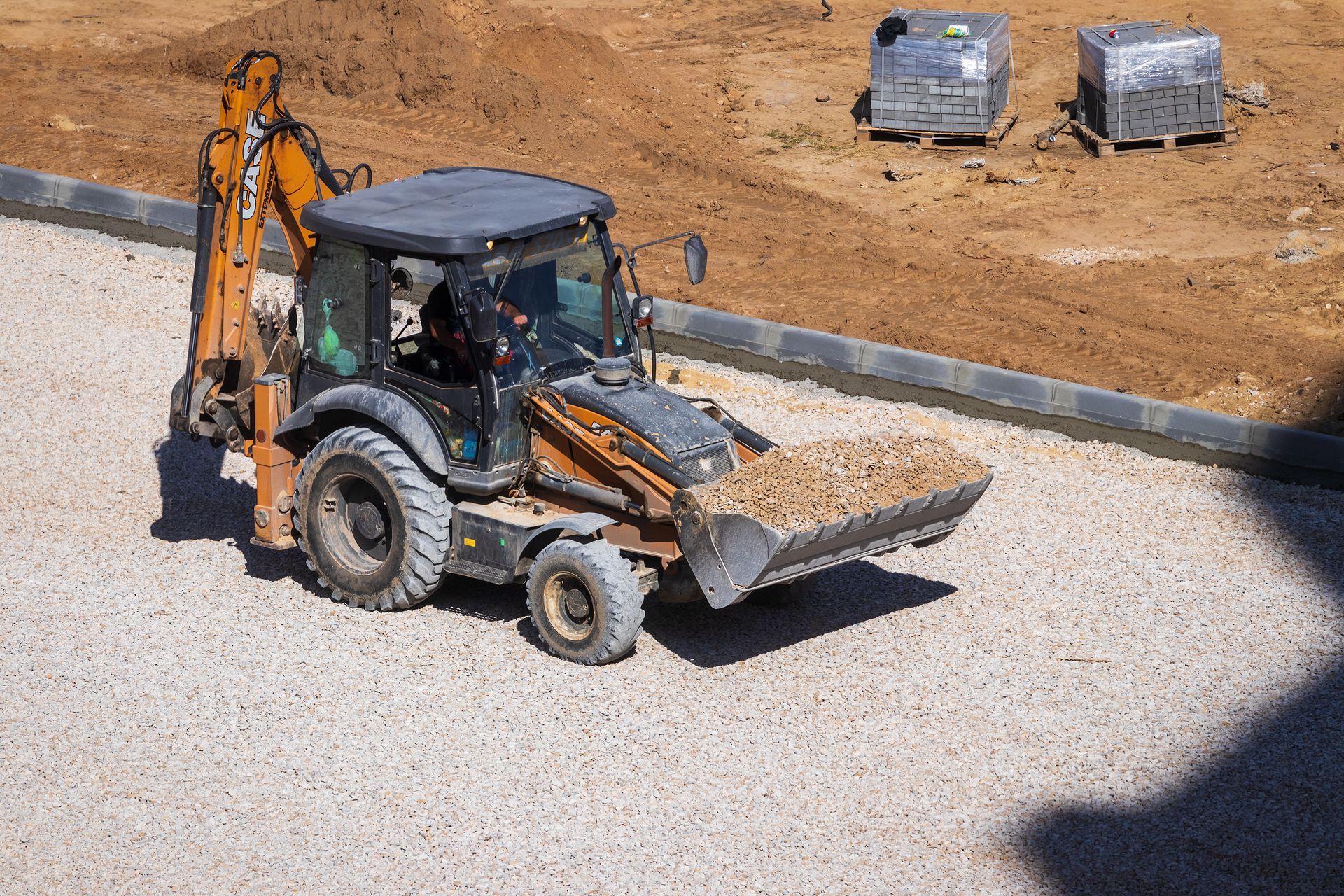 Backhoe loader on gravel, scooping up material on a construction site.