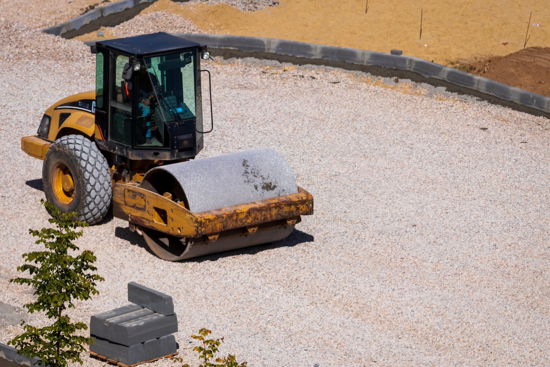 A yellow road roller compacting gravel on a construction site.