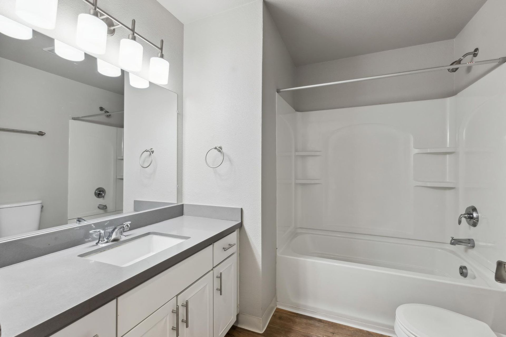White bathroom with a single vanity, large mirror, and a bathtub/shower combo at Villa Palms Apartments.