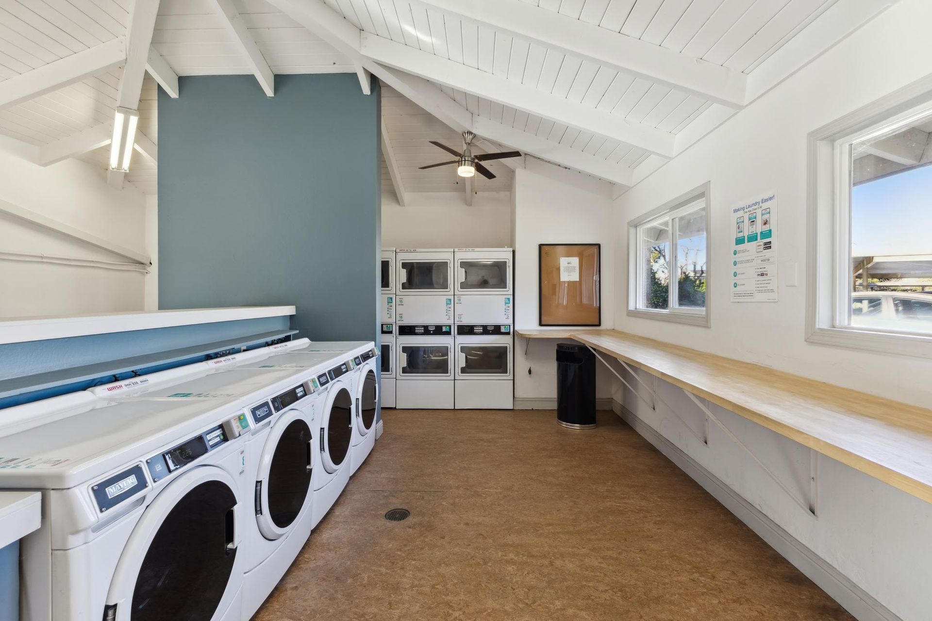 Communal laundry room with front-loading washers and dryers, a long wooden counter, and high vaulted white ceilings at Villa Palms Apartments.