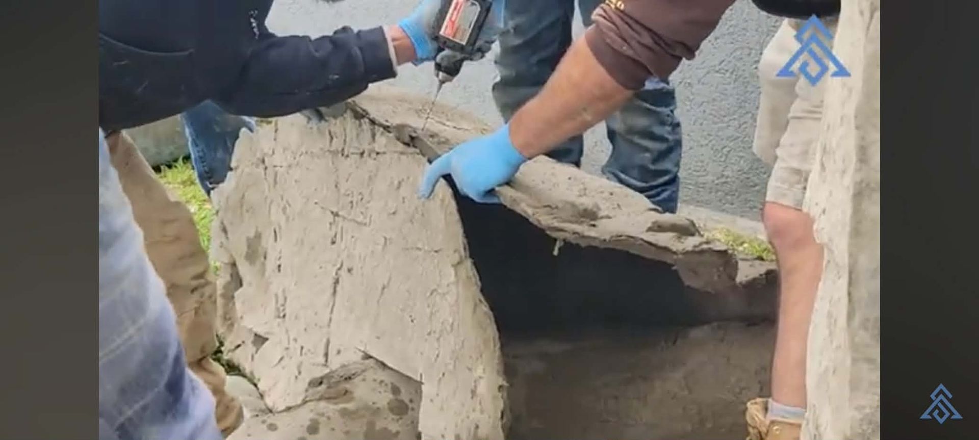 People in gloves lift a broken concrete slab at a construction site.