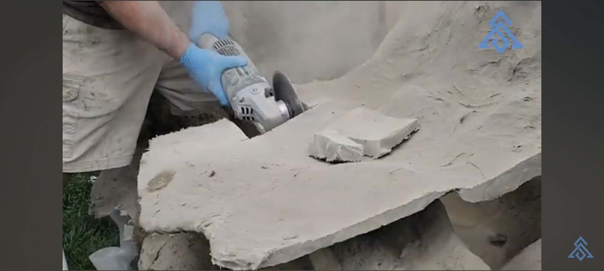 Person using a power tool to cut a large stone slab, with dust and debris around the work area