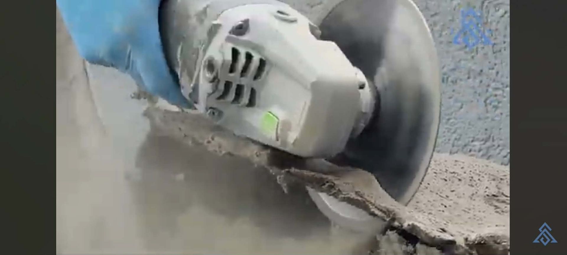 Close-up of a concrete saw cutting pavement, sending up dust and debris.