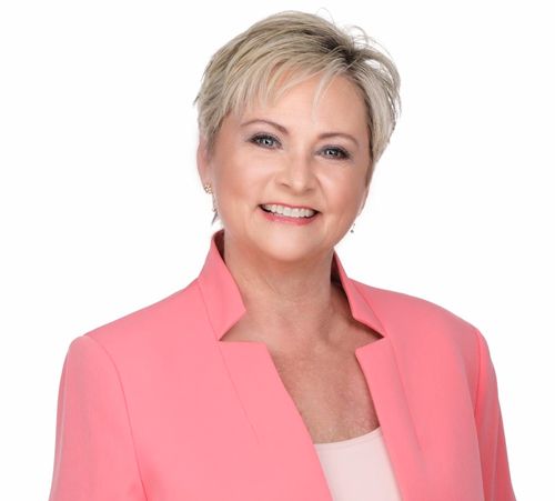 A woman in a pink jacket is smiling for the camera.