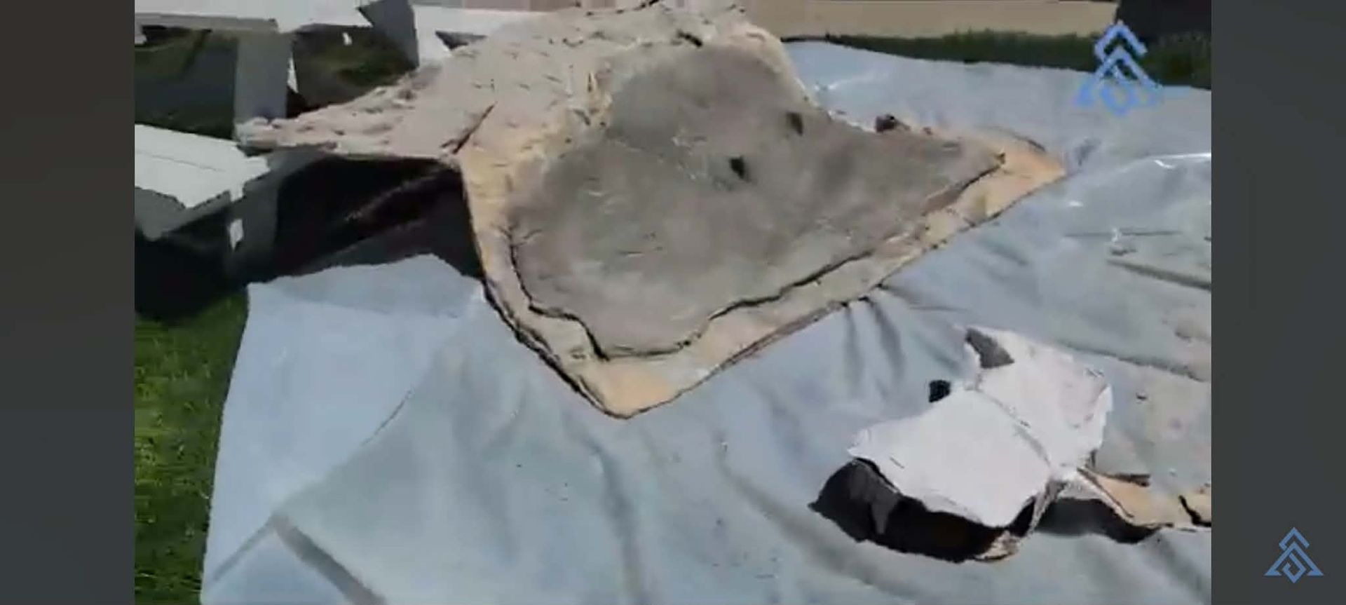 Large gray cloth draped over a table outdoors, with small white items nearby and grass in the background