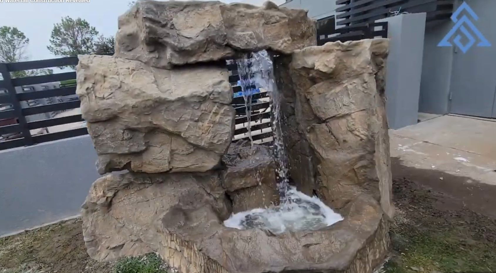 Rock waterfall fountain built into faux stone, water flowing into a small basin outdoors