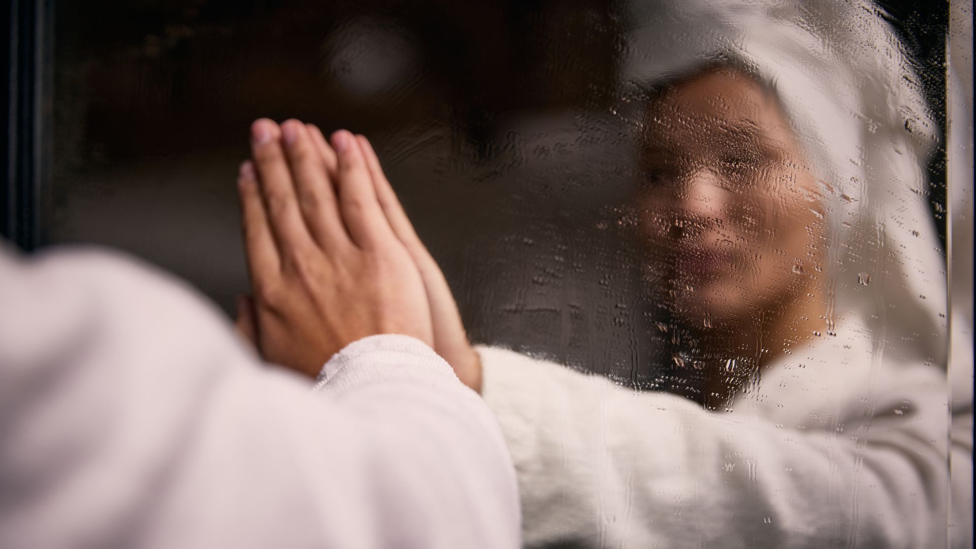 Person in a towel touching a foggy mirror with visible condensation in bathroom.