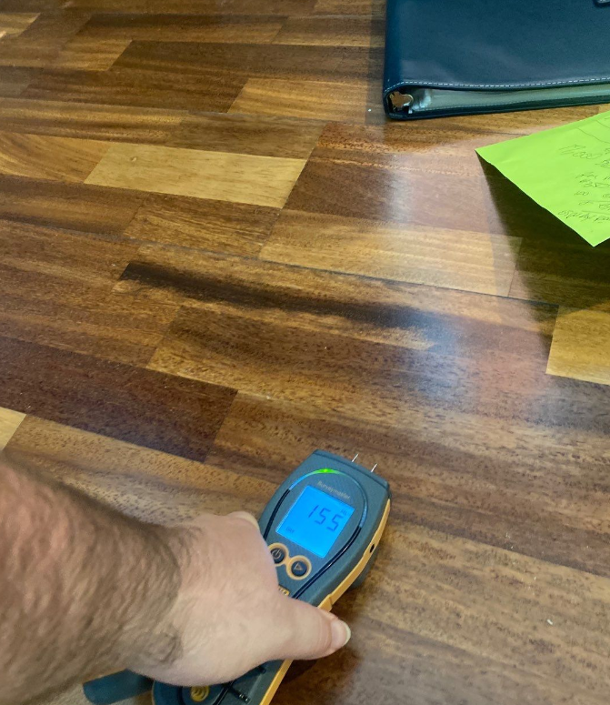 A person is holding a thermometer on a wooden floor.