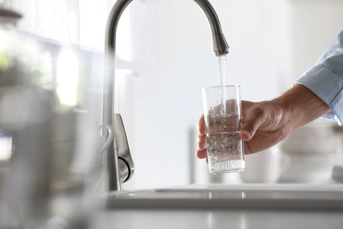A person is pouring water into a glass from a faucet.