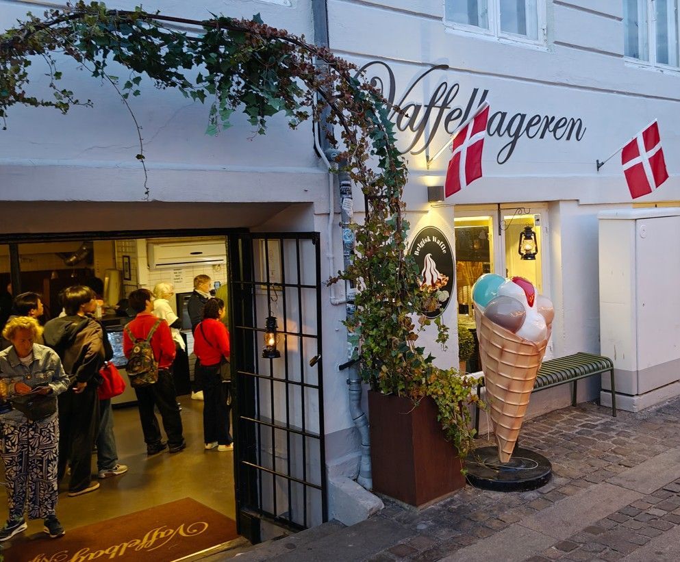 Ingang van een ijssalon met Deense vlaggen, een bloemenboog en klanten in de deuropening.