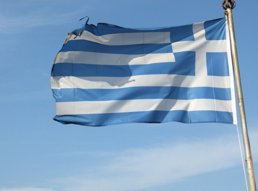 De Griekse vlag wappert in de wind tegen een blauwe hemel. Witte en blauwe horizontale strepen met een wit en blauw vierkant linksboven.