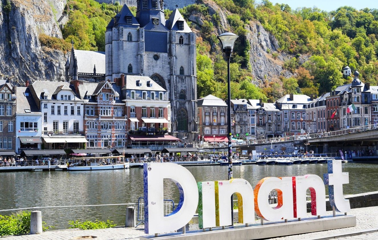 De waterkant van Dinant met de rivier, de brug, gebouwen tegen de klif en een groot 