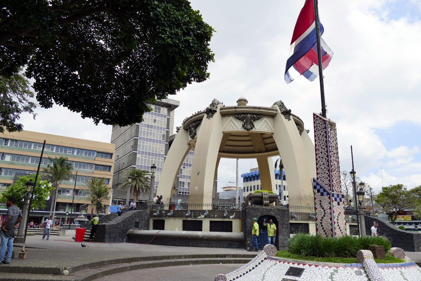 Een prieelachtige constructie op een plein, met de Costa Ricaanse vlag erboven. Mensen lopen rond in de buurt van gebouwen.