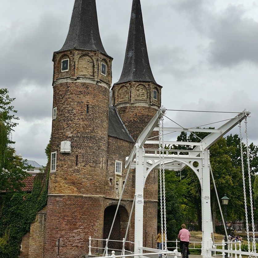 Twee bakstenen kasteeltorens met donkere spitsen naast een witte ophaalbrug onder een bewolkte hemel.