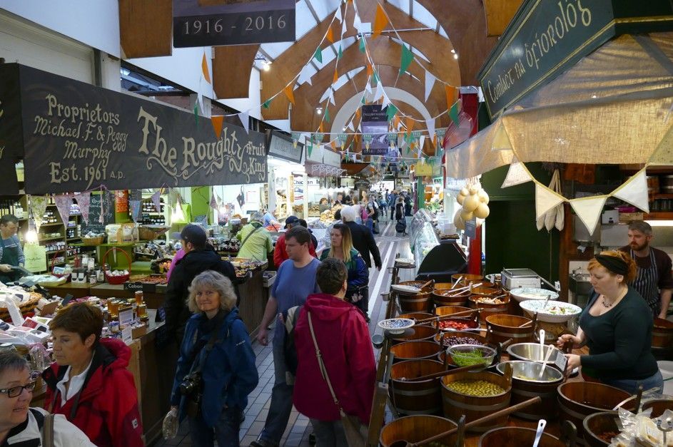 Een drukke markt met veel mensen die langs de kraampjes slenteren onder een houten gewelfd plafond.