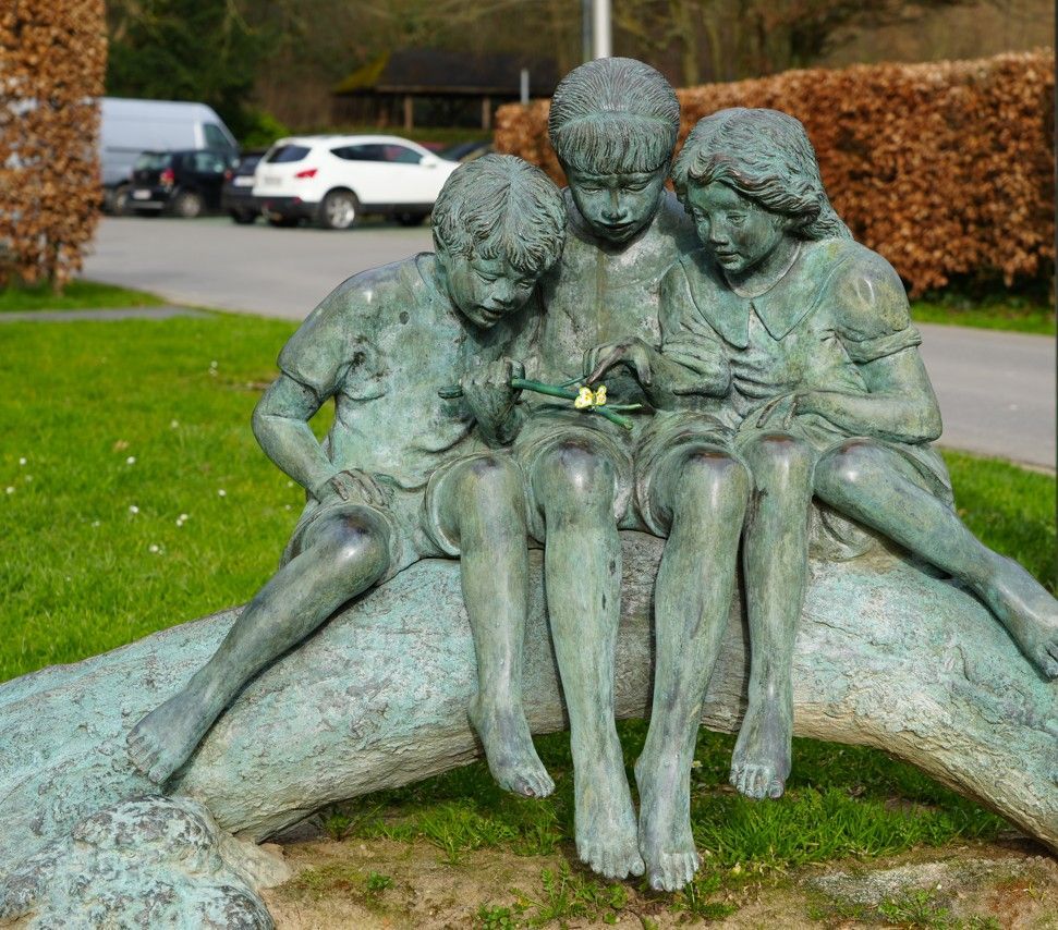 Een bronzen sculptuur van drie kinderen die samen op een omgevallen boomstam zitten.