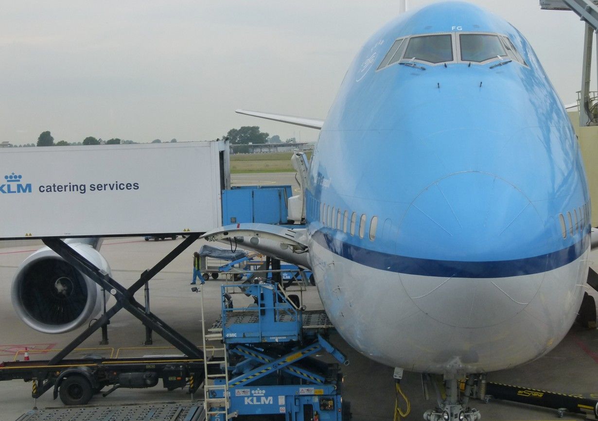 Een KLM Boeing 747-vliegtuig staat aan de gate en wordt geladen met vracht. Blauw-witte kleuren.