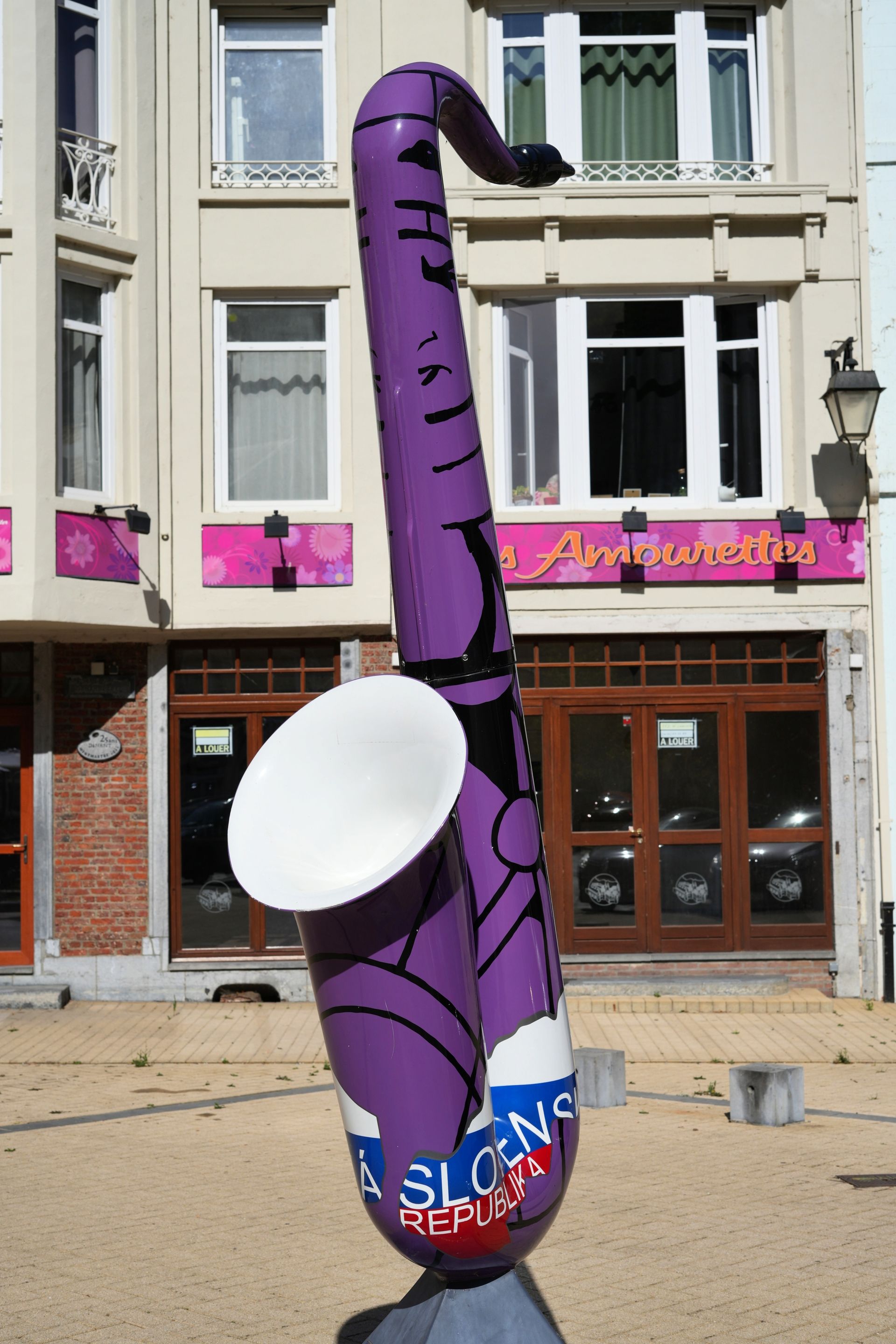Paarse opblaasfiguur in de vorm van een saxofoon buiten een winkelpand met roze uithangbord.
