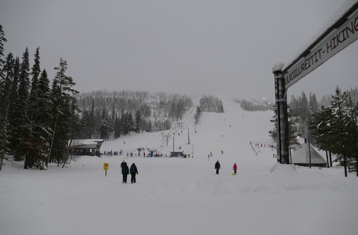Besneeuwde skipiste met skiërs en een bord met informatie over activiteiten.