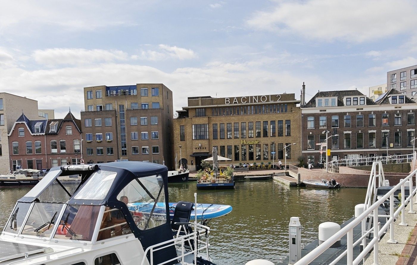Een jachthaven aan het kanaal met boten, een witte brugleuning en bakstenen gebouwen langs de waterkant.