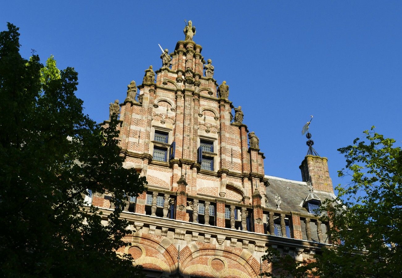 Een sierlijk bakstenen gebouw met een zadeldak, versierd met houtsnijwerk en ramen, tegen een helderblauwe hemel.