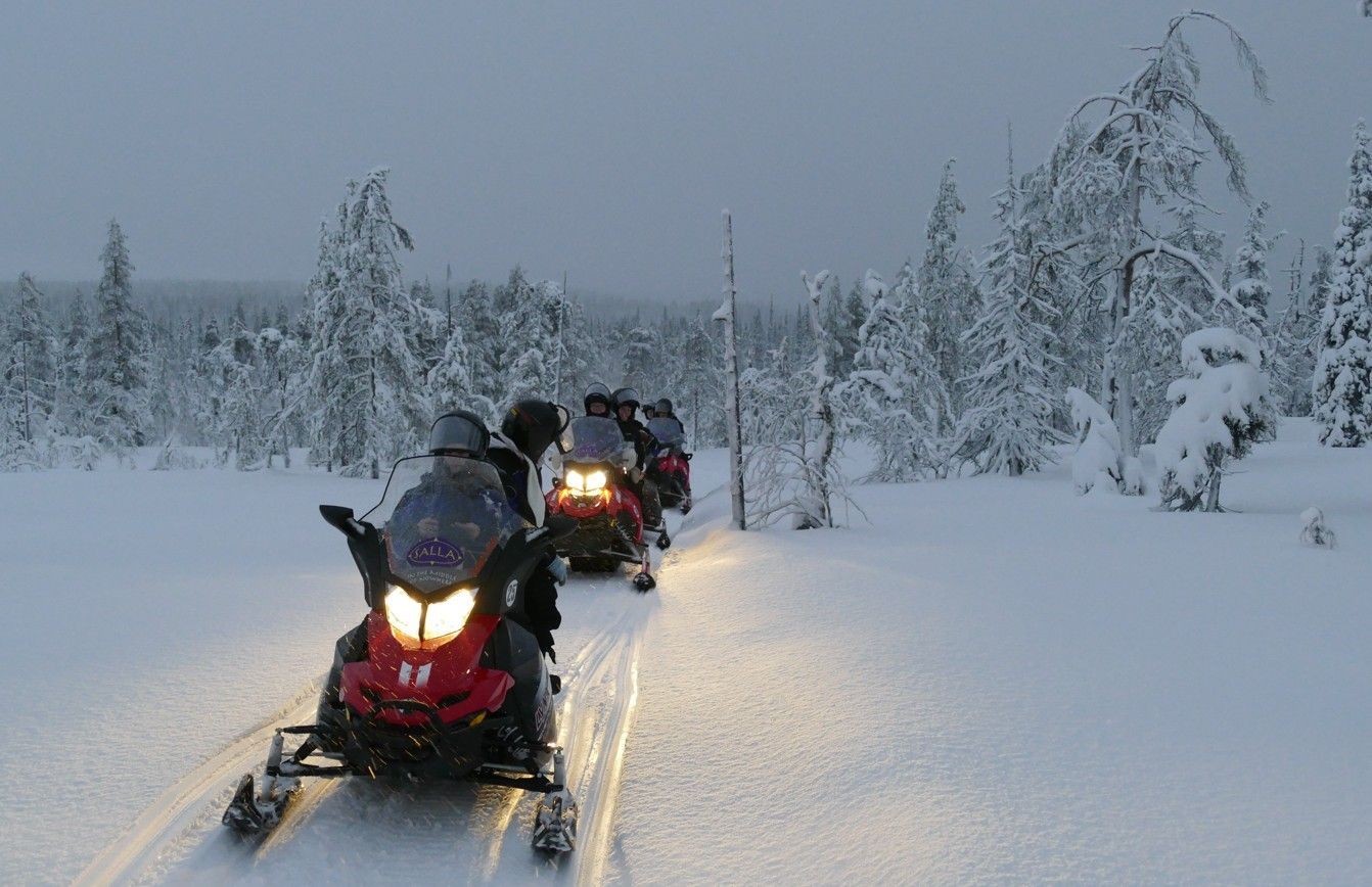 Sneeuwscooters rijden door een besneeuwd bos in de schemering.