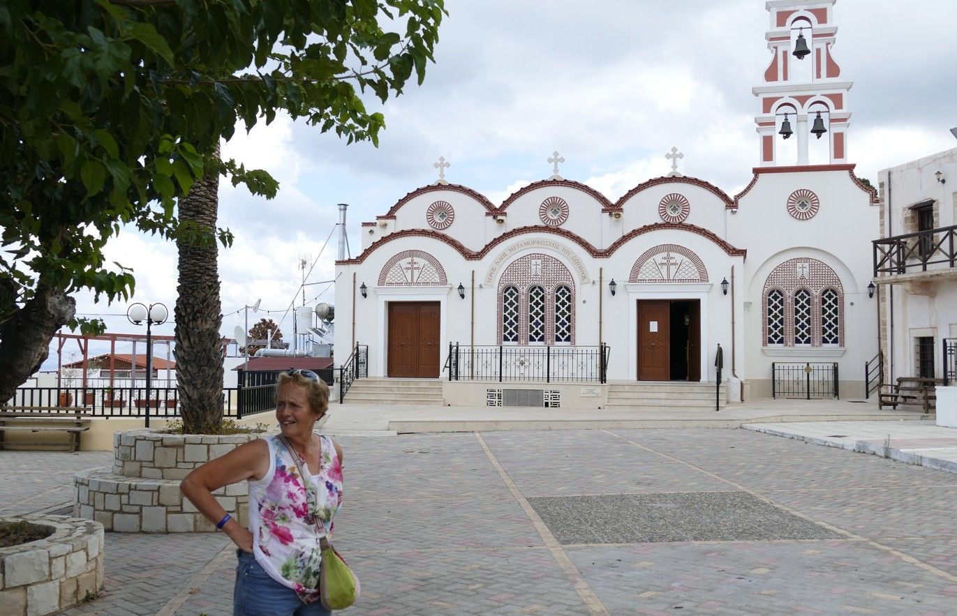Vrouw voor een witte kerk met gewelfd dak en klokkentoren. Bewolkte lucht, geplaveide binnenplaats.
