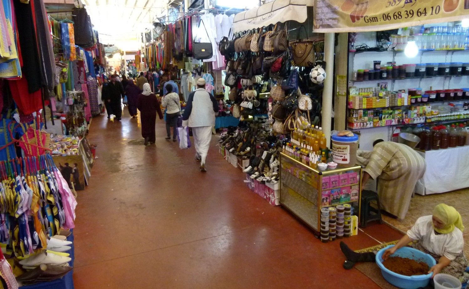 Een levendige marktplaats met verkopers die hun waren aanbieden; mensen die door de gangen lopen.